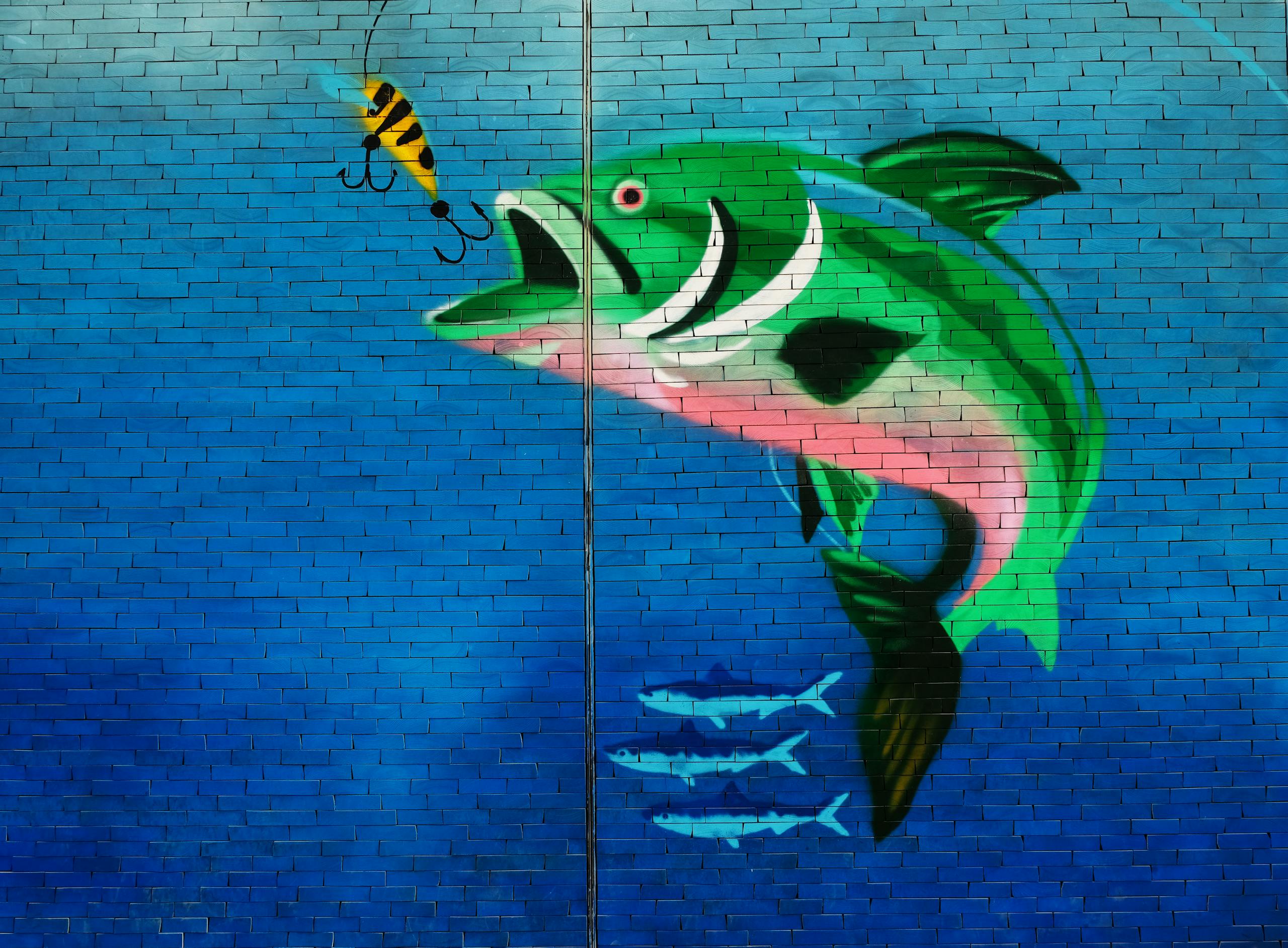 Vibrant mural of a fish and bait on a brick wall, showcasing street art in Dubai.